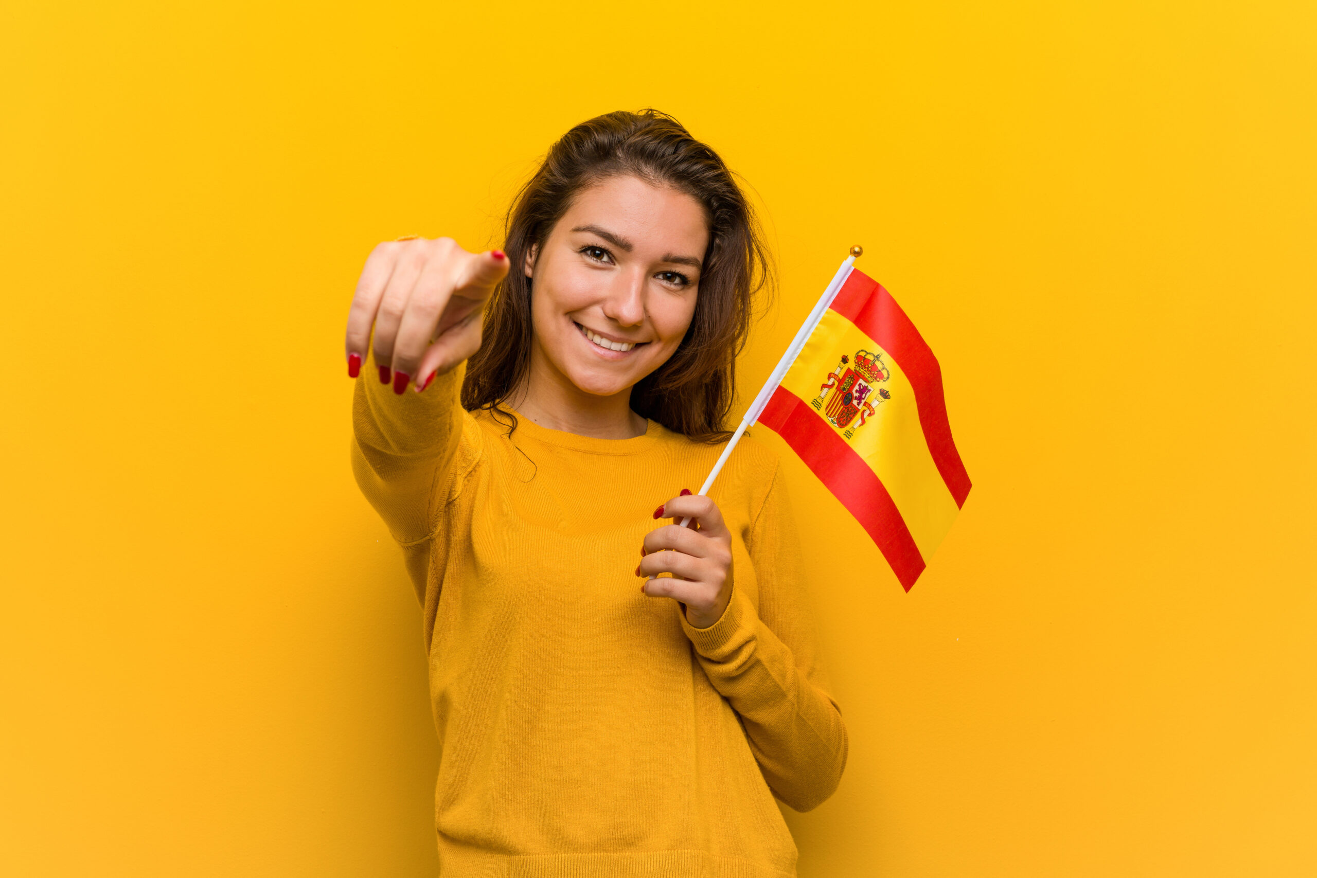 Kobieta ucząca się jęzka hiszpańskiego trzyma flage tego kraju w dłoni